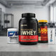 Grupo de suplementos deportivos: Optimum Nutrition Whey Protein, GAT Creatina, Mutant Mass Gainer y Shaker en el mostrador del gimnasio.